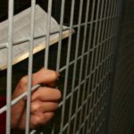 Bible and praying hands behind bars