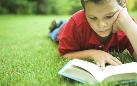 boy reading a book in the summertime