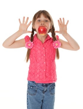 Little girl with hands raised & apple in mouth.